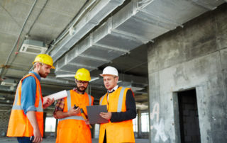 Trois architectes en gilet orange et portant des casques travaillent sur un chantier