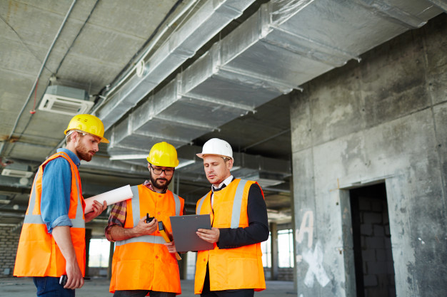 Trois architectes en gilet orange et portant des casques travaillent sur un chantier